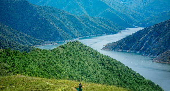 Photo of a woman in front of beautiful blue green Kozjak lake surrounded by hills in the mountains of North Macedonia.