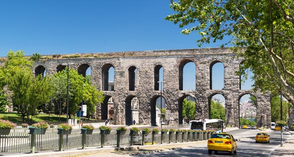 Aqueduct of Valens over city road, Istanbul, Turkey. It is old landmark of Istanbul. Cars drive on street in Fatih district in summer. Ancient Roman architecture, historic building in Istanbul town.