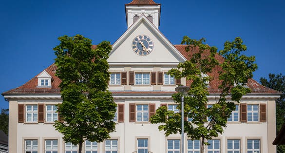 photo of view of Old school house also used as the local city hall with trees in foreground in Waldhilsbach, a small village near Heidelberg in Baden-Württemberg Germany.