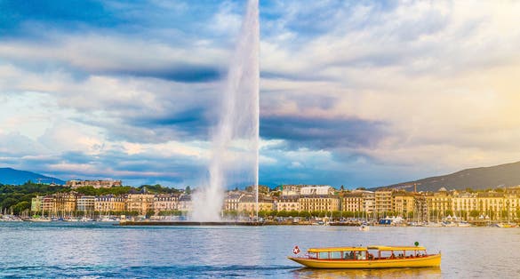 Photo of panoramic view of Geneva skyline with famous Jet d'Eau fountain and traditional boat at harbor district in beautiful evening light at sunset, Canton of Geneva, Switzerland.