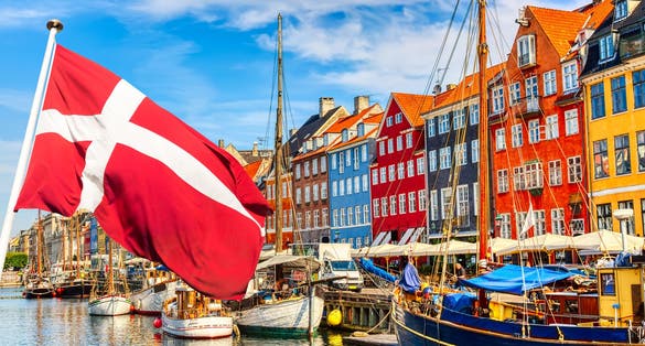 Copenhagen iconic view. Famous old Nyhavn port in the center of Copenhagen, Denmark during summer sunny day with Denmark flag on the foreground.