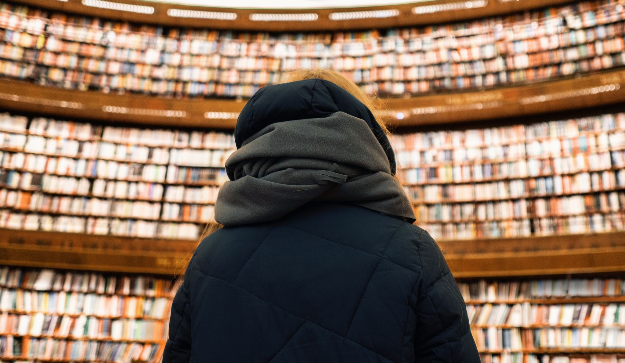 photo of a girl in a scarf in the Stockholm Public Library against the backdrop of several floors of books in Sweden.