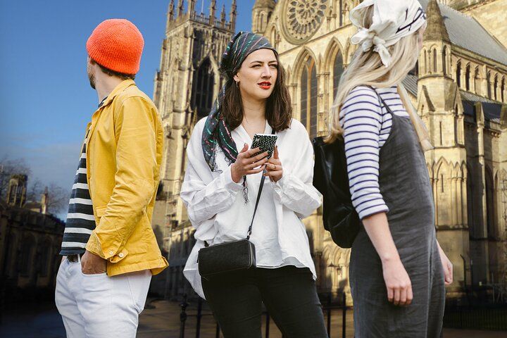 Three casually dressed tourists near York Minster cathedral, with one holding a phone and looking curious..jpg