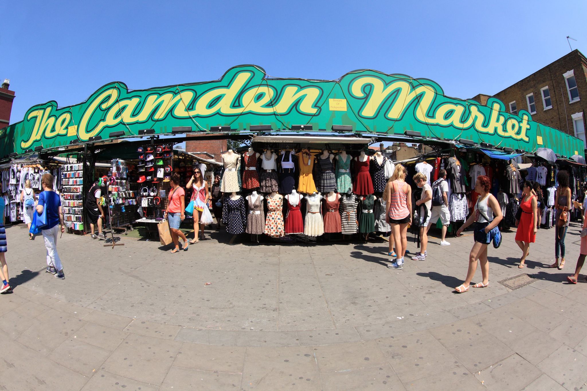 Shoppers browsing clothing stalls at Camden Market under a bright green sign on a sunny summer day..jpg