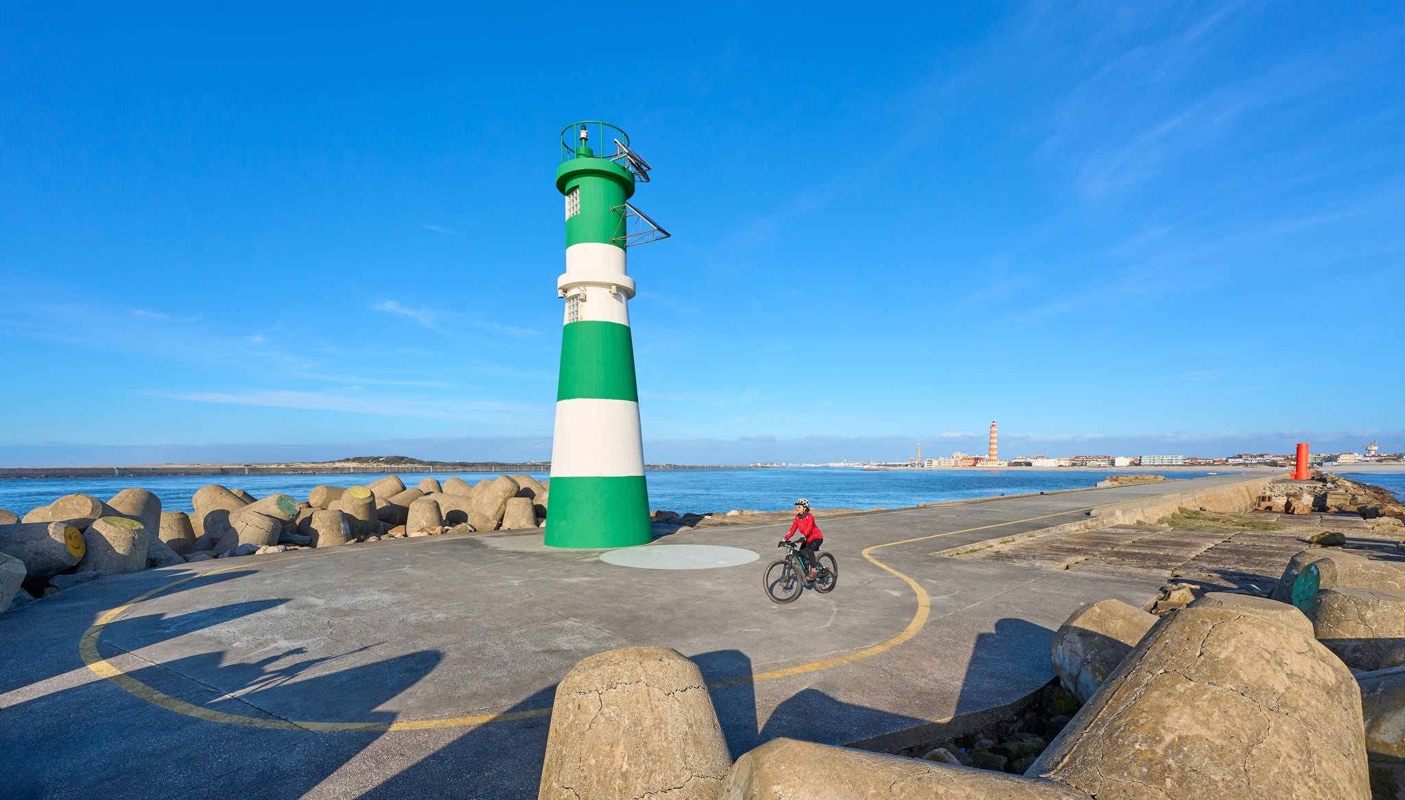 happy senior woman cycling below the navigation sign and ligthouse of Barra at the harbor entrance of Aveiro, Portugal