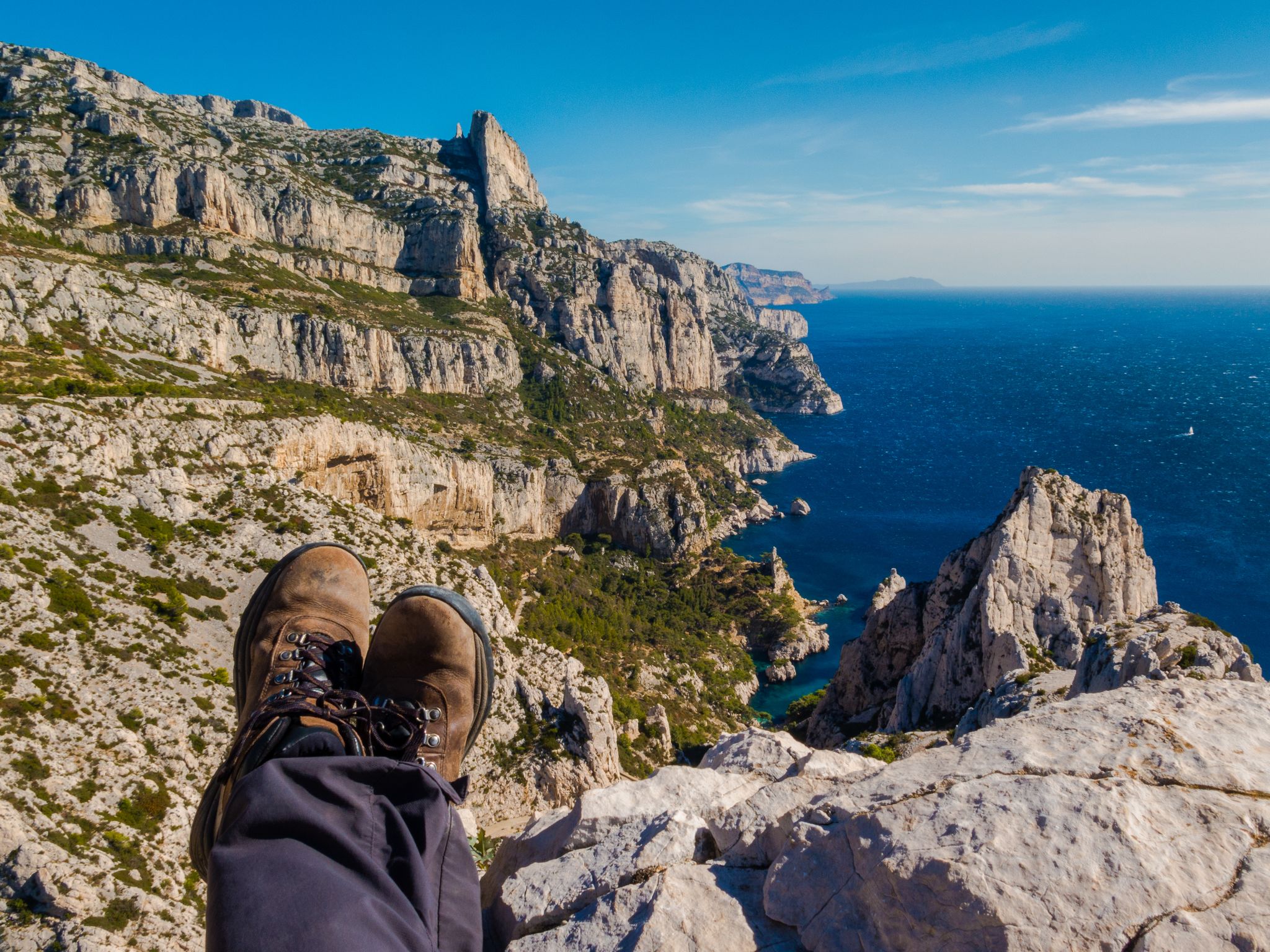 Hiker’s feet resting on a rocky cliff with panoramic view of Calanques National Park and the Mediterranean Sea near Marseille, France..jpg