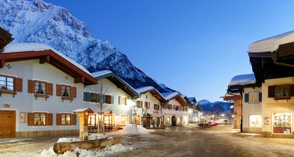 Photo of scenery of a street flanked by old chalet houses in blue twilight on a cold snowy winter evening in Mittenwald, Germany.
