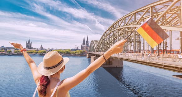 Photo of happy tourist girl holding a German flag against the Rhine bridge and Cologne Dom Cathedral. 