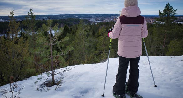 photo of view of Young girl walking with snow shoes looking over vast landscape in horizon. View over Skellefteå, Sweden.