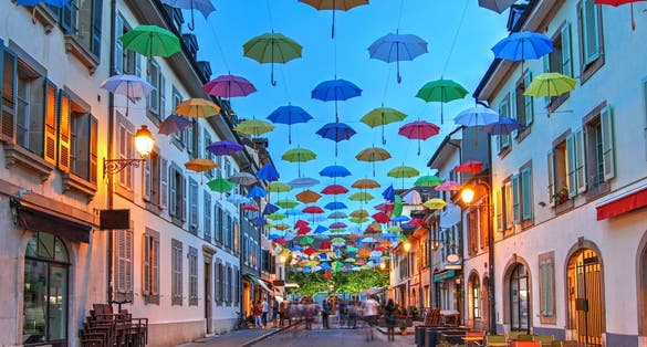 Photo of night scene in Carouge, Geneva, Switzerland along Rue Saint Joseph covered by colorful umbrellas.