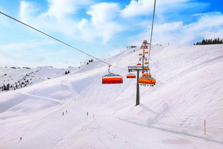 Photo of chair ski lift with orange bubble shelter and ski slope in Saalbach resort, Austria.