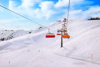 Photo of chair ski lift with orange bubble shelter and ski slope in Saalbach resort, Austria.