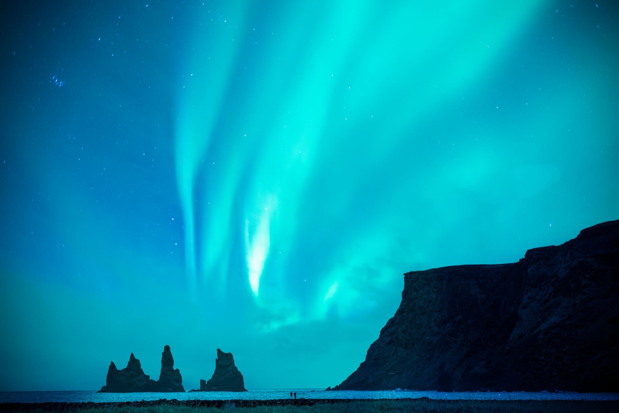 photo of a couple or lover is watching blue and green aurora borealis or northern light at black sand beach and reynisdrangar basalt rock during night sky in winter in Iceland,Europe.it is beautiful landscape.