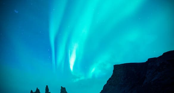 photo of a couple or lover is watching blue and green aurora borealis or northern light at black sand beach and reynisdrangar basalt rock during night sky in winter in Iceland,Europe.it is beautiful landscape.