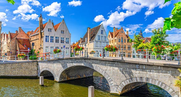 Carmersbrug Carmelite Bridge across Langerei canal, stone arch bridge with flowers on fence, old houses on embankment, Brugge old town district, Bruges city historical center, West Flanders, Belgium