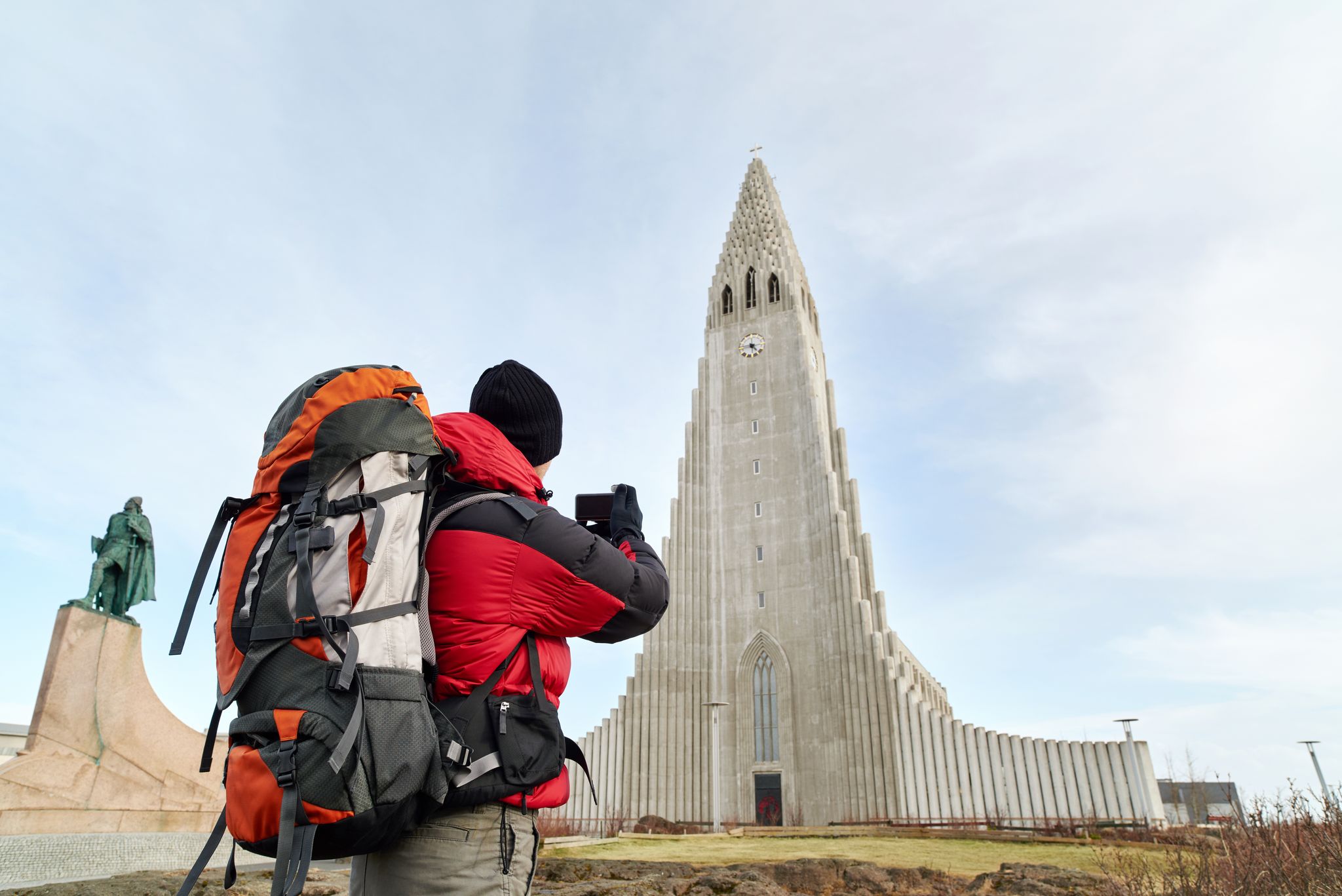 photo of rear view adventure travel backpack man taking pictures of the hallgrimskirkja cathedral in Reykjavik Iceland.