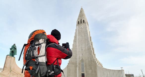 photo of rear view adventure travel backpack man taking pictures of the hallgrimskirkja cathedral in Reykjavik Iceland.