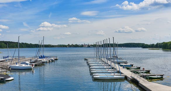 Beautiful landscape presenting sailboats and motorboats moored to the pier in the bay of the lake in the port against the background of clouds and blue sky on a sunny day in Olsztyn in Warmia and Mazu