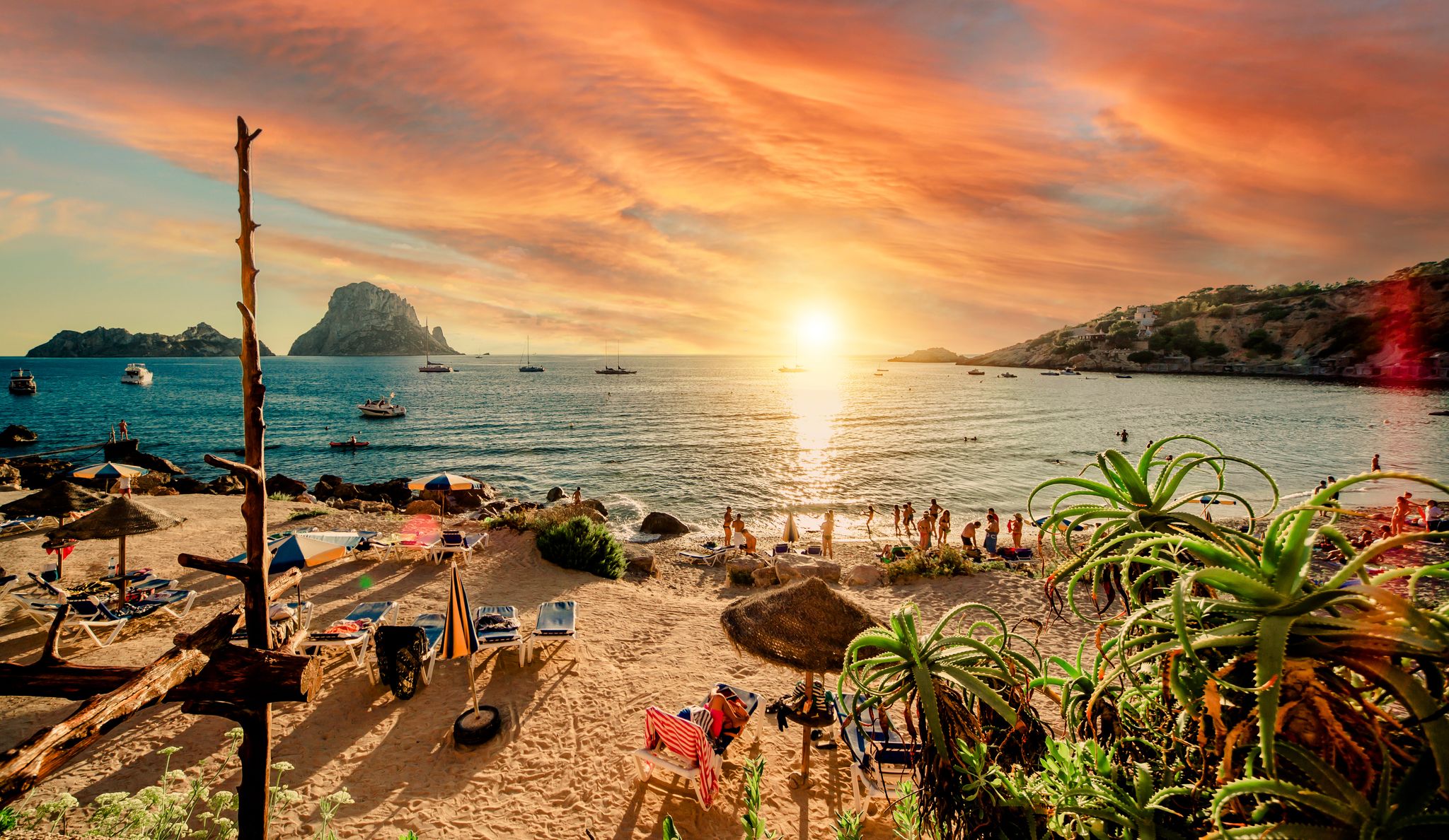 photo of Picturesque view of Cala d'Hort tropical Beach, people hangout in beautiful beach with Es Vedra rock view during magnificent vibrant sunset glowing sun. Balearic Islands, Spain.