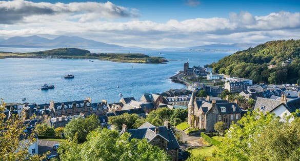 photo of view of Aerial view of small town Oban in Scotland. Scattered trees, small village and sea in the background, bright sunny day.