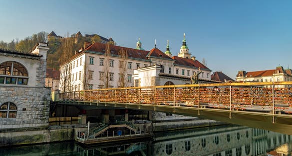 Photo of Butcher bridge with love padlocks, Saint Nicholas Cathedral and Ljubljana castle in the background.