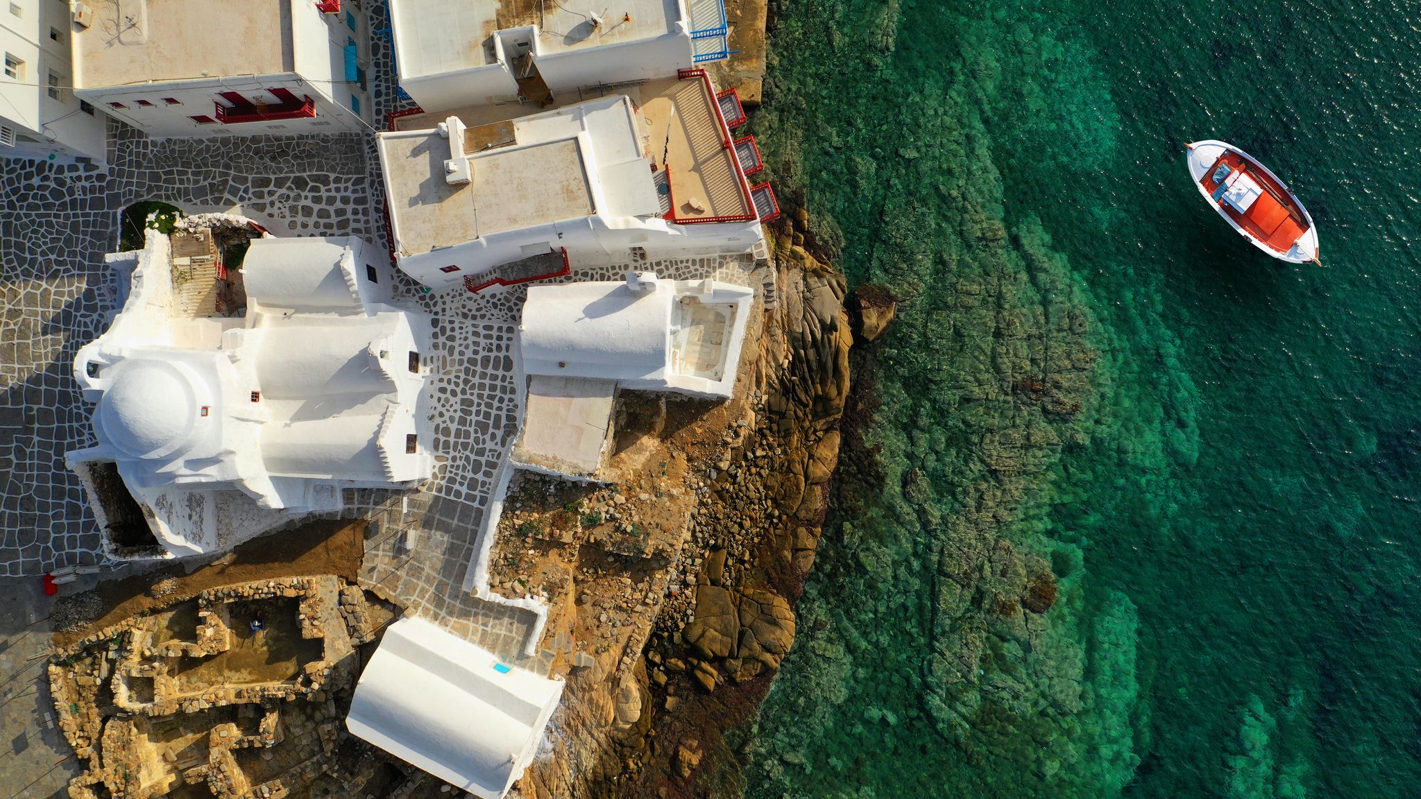 photo of view ofAerial drone top down photo of picturesque fishing boat near chapel of Paraportiani in iconic little Venice of Mykonos island, Cyclades, Greece.