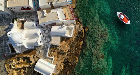 photo of view ofAerial drone top down photo of picturesque fishing boat near chapel of Paraportiani in iconic little Venice of Mykonos island, Cyclades, Greece.