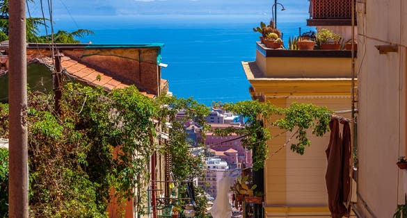 Photo of The neighborhood called Quartieri Spagnoli in Naples, Italy. Street view of old town. Narrow street of Napoli. Bright sunny day. Gulf of Naples, blue sky, sea on background. Cacti on the terrace.