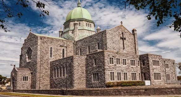 Galway Cathedral on a sunny day, Rich blue cloudy sky, Nobody. Galway city landmark, Ireland. Framed by dark tree branches at the top.