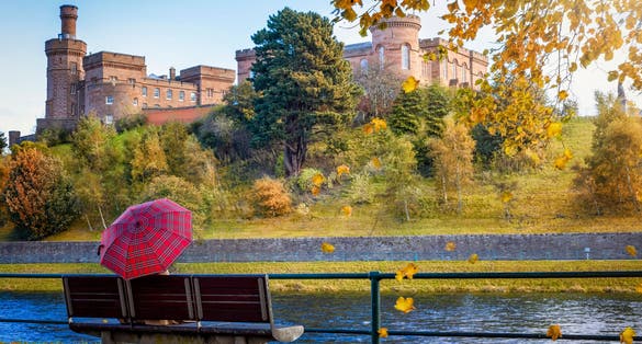 Photo of tourist woman holding a scottish flag umbrella enjoys the view of the skyline of Inverness during a sunny autumn day, Scotland.