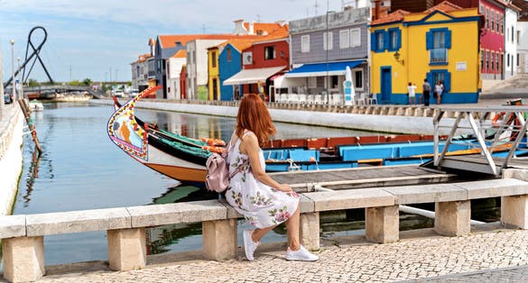 A woman traveler with red hair seat near traditional boats on main city canal in Aveiro, Portugal
