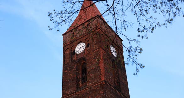 photo of view of Clock tower in the old town. Clock in Poland, Lubin. European architecture of the past. The clock tower on the background of the blue sky behind the tree branches