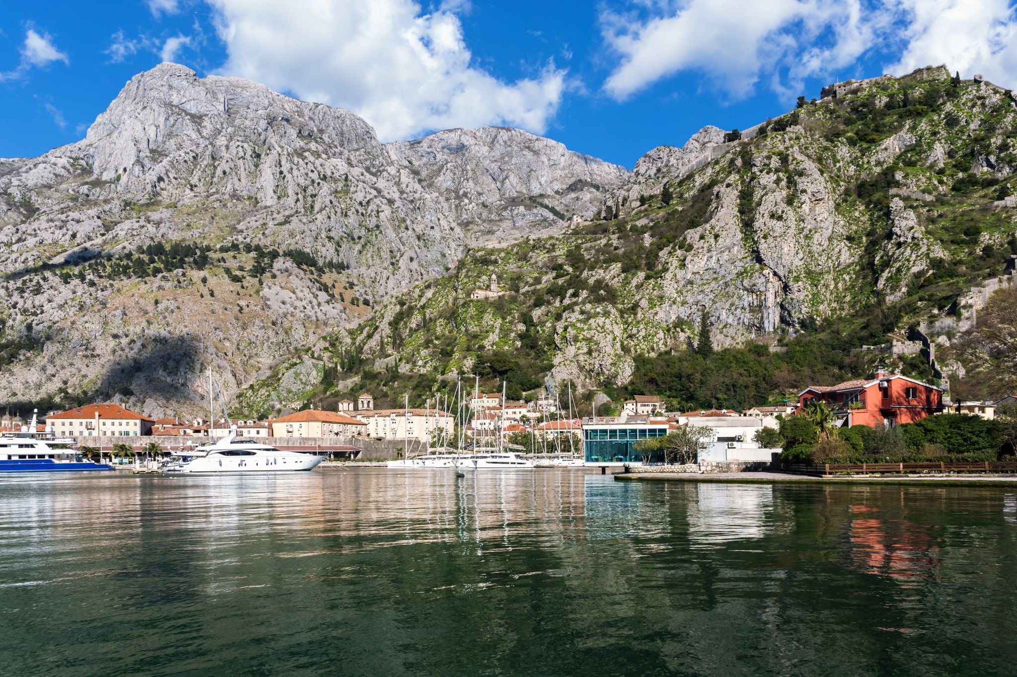 Photo of Kotor marina. Clear view with vibrant blue waters and Kotor fortress in the mountainous backdrop. Montenegro.