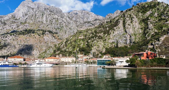 Photo of Kotor marina. Clear view with vibrant blue waters and Kotor fortress in the mountainous backdrop. Montenegro.