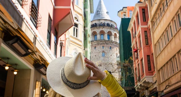 Beautiful young tourist girl in fashionable clothes poses with view of landmark Galata tower in Beyoglu,Istanbul,Turkey.