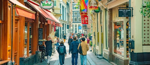 Pedestrians walking through a colorful shopping street in Amsterdam with Pride flags in August..jpg