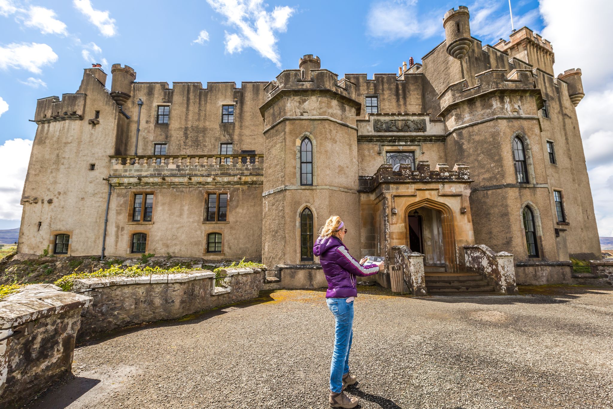 Photo of Smiling young woman tourist looks at the brochure of Dunvegan Castle, Dunvegan, Isle of Skye, Scotland, UK on a sunny day.