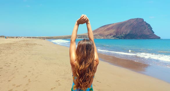 Photo of back view of beautiful woman doing stretching exercises on the beautiful beach in Playa La Tejita, Tenerife.