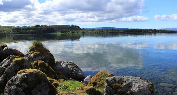 photo of Lake Þingvallavatn at Iceland with ice cold crystal water and fantastic view on clouds at sky and water surface from the rocks with grass.