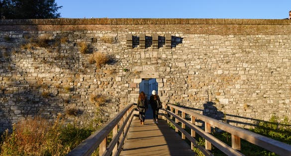 Outdoor of wooden pedestrian bridge cross Jeker canal and small gate entrance of Nieuwenhofstraat Defensive Wall in Autumn season, in Maastricht, Netherlands during evening sunset time.