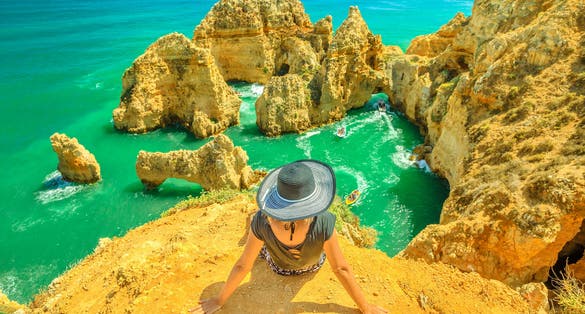 Photo of  tourist sitting on promontory of Ponta da Piedade, woman looking amazing views of iconic cliffs of turquoise sea of Lagos.