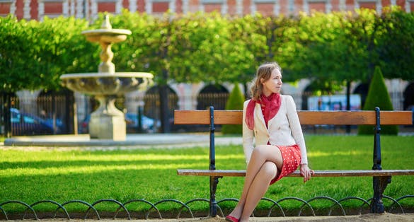 photo of beautiful young woman in red polka dot dress sitting on bench at Place des Vosges in Marais, Paris, France.
