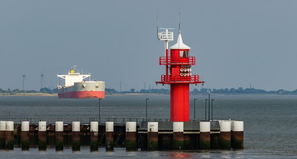 Photo of Red lighthouse at the Brunsbuettel lock with cargo ship in the background, Schleswig-Holstein, North Sea, Germany.