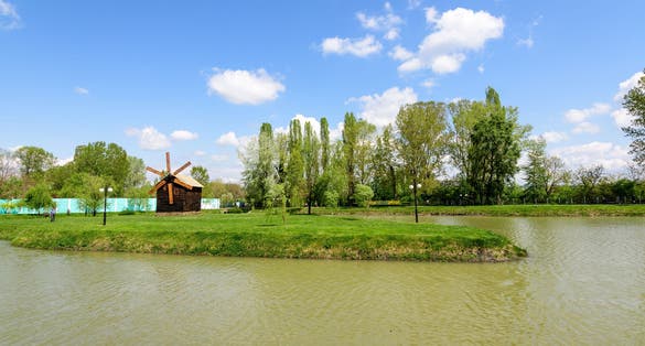 Small lake with a woodmill and an island from Chindiei Park (Parcul Chindiei) in Targoviste, Romania, in a sunny spring day with white clouds and blue sky