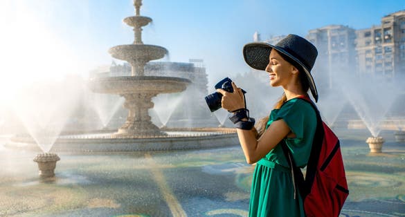 Young female traveler photographing central fountain in Bucharest city, Romania.