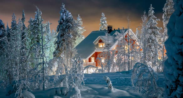 Photo of beautiful winter night landscape with deep snow covered trees and wooden hut in foreground, Finland.