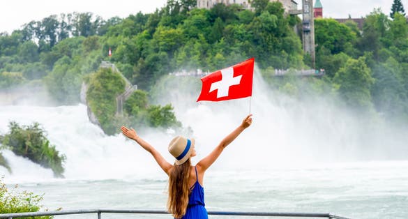 Photo of female tourist with swiss flag in front of the famous Rhine waterfall in Switzerland.