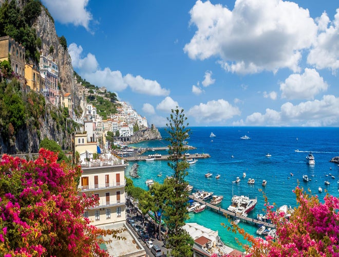 Amalfi Coast in June with colorful flowers, boats in turquoise water, and hillside buildings under sunny skies..jpg