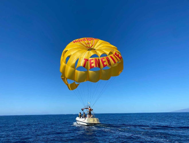 A yellow parasail with Tenerife written on it is attached to a boat floating above the blue ocean in Costa Adeje..jpg