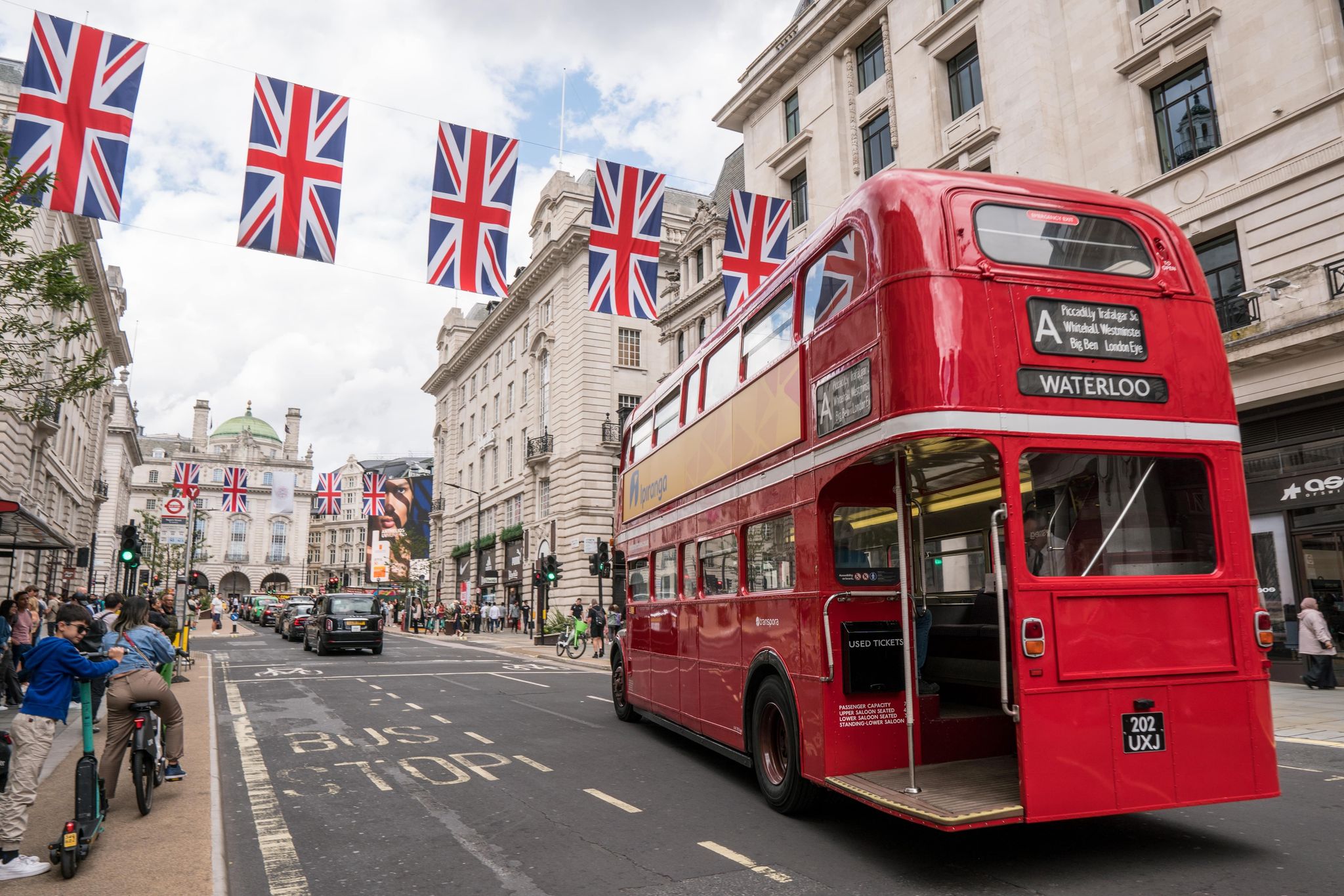 Iconic red double-decker bus driving through central London under rows of Union Jack flags..jpg
